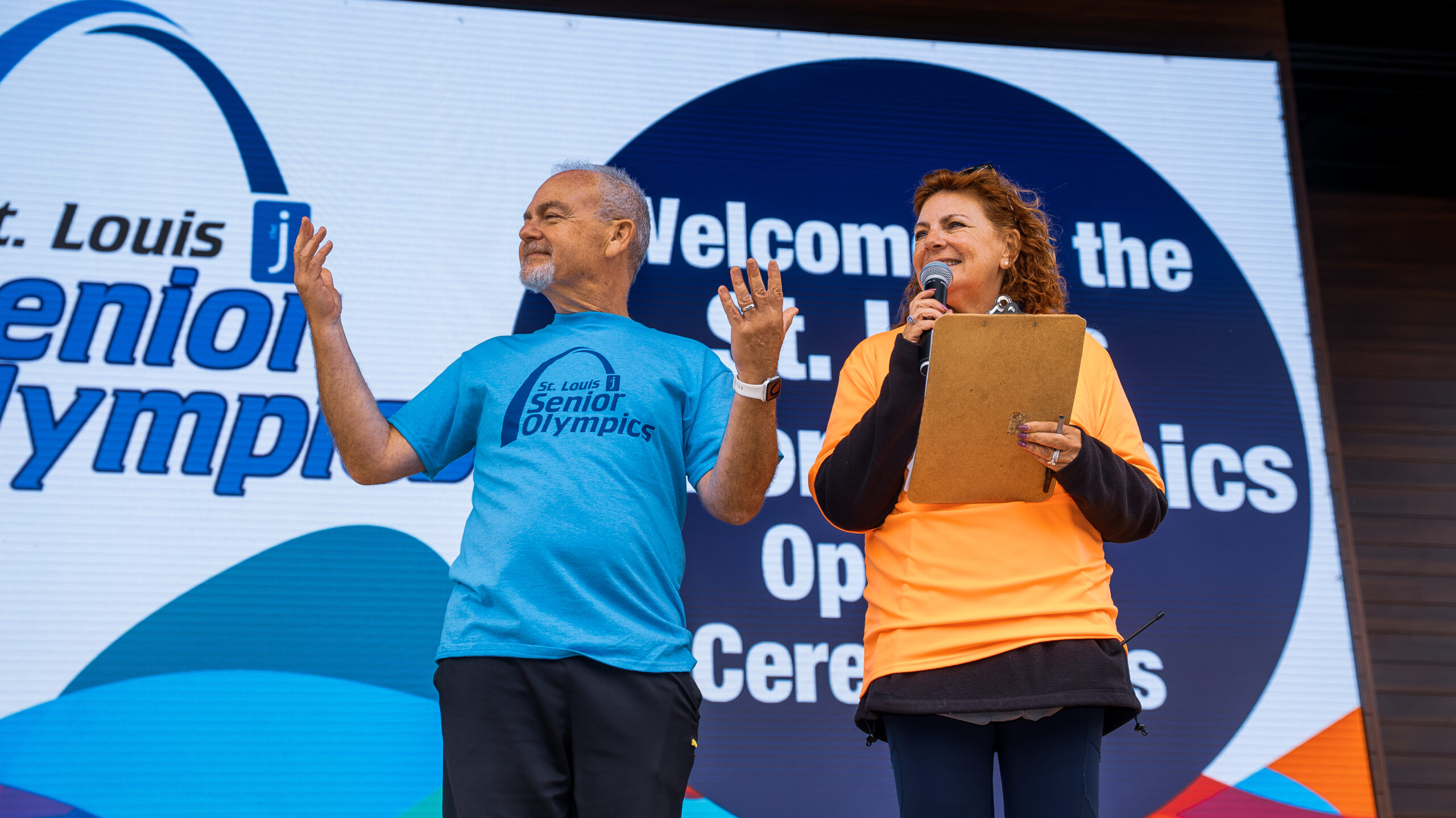 Two volunteers, man and a woman, where orange and blue St. Louis Senior Olympics T-shirts.