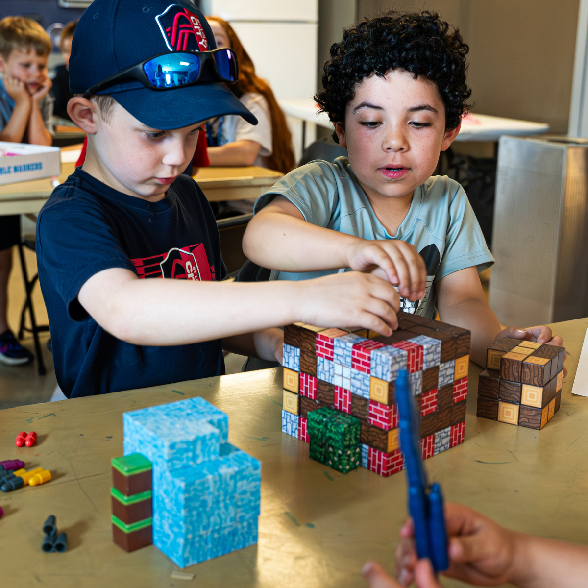 Photo from J Day Camps 2025 at The J - St. Louis: two campers, boys of perhaps 7 or 8, create Minecraft-like paper building cubes.